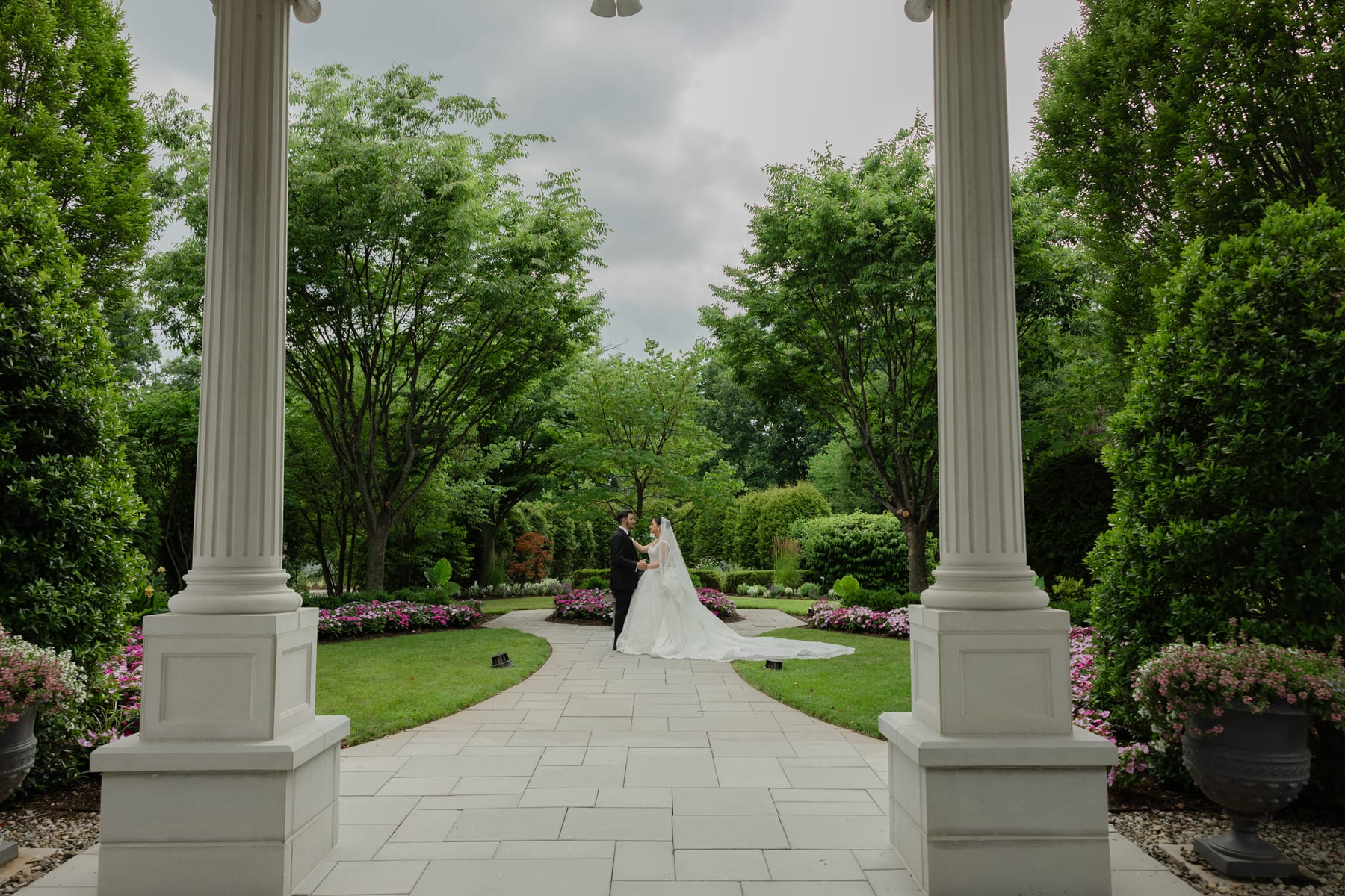 The bride and groom together in a garden framed by white columns